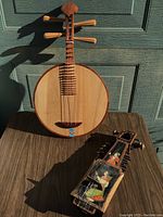 Photo showing both instruments on a wooden surface with natural sunlight highlighting the Ruan's round wooden body and the painted Surbahar's detailed artwork.