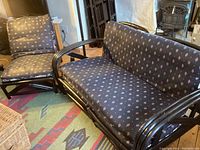 Black painted tiki cane love seat and chair with black fabric cushions featuring small floral patterns set on a colorful rug.