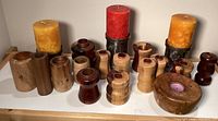 Front display of fourteen wooden candle holders of assorted sizes and designs, three metal candle holders with large pillar candles.