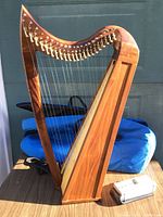 Full front view of wooden lap harp standing on table with blue padded case behind and silver tuner box to right