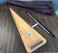 Full view of the light wood zither with bow and carrying case on a wooden surface