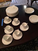 Eight stacked dinner plates, two soup bowls, five bread plates, six cups with saucers arranged on a dark wood table