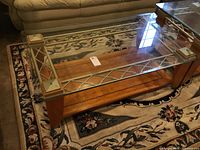 Photo showing rectangular glass top coffee table on floral carpet with wooden base and metal lattice support, visible scratches on base.