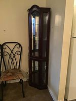 Lighted corner curio cabinet in a room next to chair, showing front and side glass panels and door.