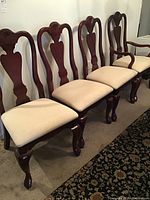 Six dark wood dining chairs aligned against wall, two armchairs at one end. Cream upholstered cushions, carved backs and cabriole legs visible.