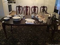 Full view of the dining table with leaf and six chairs, showing wooden polished surface and chairs with cushions.