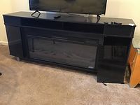 Front view of black electric fireplace media center with electric fireplace insert, two-glass cabinets on sides, flat top with TV and remotes visible.