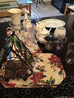 Full view of table displaying the lot items including Lenox vase, floral platter, porcelain candle holder, various glassware, wine rack, placemats, and tea accessories.