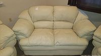 Front view of cream leather loveseat, showing attached cushion style and overall condition.