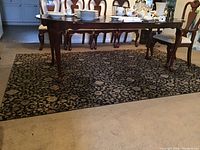 Photo of a rectangular dark floral pattern area rug under a dining table with wooden legs and chairs.