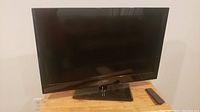 Front view of Seiki 32 inch TV on wooden table with remote beside it