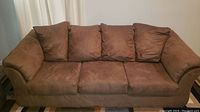 Front view of the brown Ashley Furniture sofa showing attached back pillows, seat cushions, and visible stains.