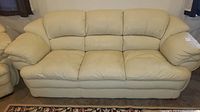 Front view of three-seat DeCoro sofa in cream beige leather-like upholstery with attached cushions and plush armrests.