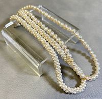 Two pearl chokers displayed on acrylic stand, showing the difference between baroque freshwater pearls and smaller faux pearls.