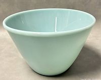 Side view of pale blue-green Fire-King glass bowl showing smooth surface and curved tapered shape.