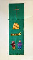 Front view of full green fabric wall hanging with embroidered red cross, igloo, sled, and Inuit figures.