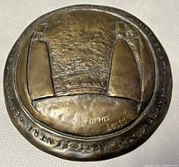 Front view of bronze medal showing abstract relief with text.