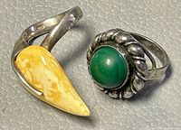 Both rings shown together on gray textured surface, highlighting yellow and green stones and 925 markings.