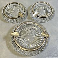Overall view of three clear crystal ashtrays with silver rims and cigarette rests, showing size difference and condition.