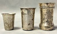 Front view of three antique silver kiddush cups showing engravings and patina