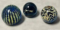 Three Mdina glass paperweights showing different patterns and sizes.