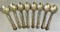 Eight sterling silver espresso spoons laid out side by side showing overall design and condition.