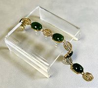 Close-up angled view of one section showing two green oval jade stones and two gold-filled Chinese character medallions.