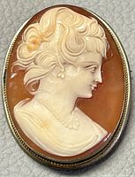 Front view of the oval cameo brooch showing carved woman profile in shell on warm brown background.