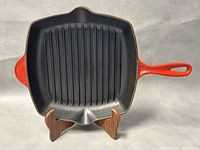 Front view of square cast iron grill skillet with black ridged interior and red-orange handle and exterior sides.