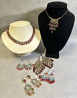 Overview of 2 choker necklaces displayed on bust forms and 4 pairs of colorful drop earrings laid out on a tabletop