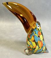 Oblique side view of the blown art glass toucan figurine showing the large amber beak and colorful mosaic body.