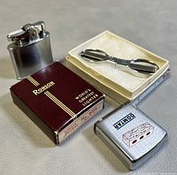 Vintage Ronson lighter with original burgundy box, Slip N Snip folding scissors in white box, and Zippo tape measure with Domtar brick graphic.