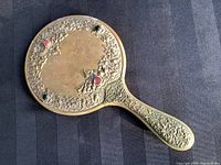 Full front view showing the brass floral detailing and colored jewels on the back of the mirror with some patina and wear.