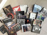 Photo showing all 22 rock music CDs laid out on a light wooden surface, covers visible, featuring various rock bands and artists.