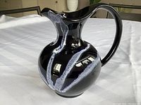 Side angle view showing the curved handle and spout, and the waved design on the body of the pitcher.