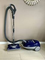 Full view of Kenmore Elegance canister vacuum, showing blue main body, hose, wand, handle, and vacuum head on light wood floor.