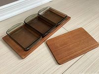 Main teak tray with three smoky shaded glass containers in place and additional smaller teak tray beside it on floor