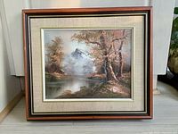 Framed landscape painting showing a mountain, lake, and trees with an autumn color palette.