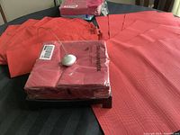 Six red placemats laid flat and stacked red paper napkins in original packaging with a patio napkin holder on top.
