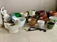 Wide view showing mix of ceramic, terracotta, plastic, and metal pots including a white chicken-shaped ceramic planter