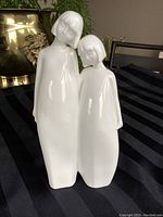 Front view of the white porcelain figurine showing two girls standing side by side, leaning close to each other affectionately.