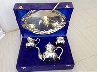 Full view of the brass tea set arranged inside the open custom purple velvet box, showing all four pieces: teapot, creamer, sugar bowl with lid, and tray.