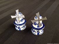 Front view of two windmill-shaped blue and white ceramic salt and pepper shakers on black fabric background.