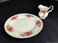 Dinner plate and creamer displayed together on a black surface showing floral pattern and gold trim