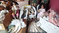 Multiple African American dolls standing on a surface, surrounded by additional doll clothing and accessories. Includes Daddy's Long Legs dolls and others with various outfits and hairstyles. The dolls are between 12 and 16 inches tall.