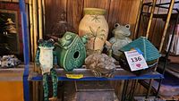 Showcases group of animal decor including green ceramic frogs with legs dangling, rustic frog sculpture, ceramic bird huts, and vases on shelf.