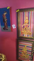 Two framed Asian needlepoint textiles with colorful striped backgrounds hanging side by side on a purple wall