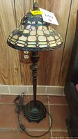 Full view of the Tiffany style table lamp showing stained glass shade and metal base on tiled floor.