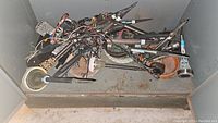 Pile of assorted landscape lighting stakes with wiring and an aftermarket car alarm system components mixed in. Metal stakes mostly black with some visible rust and dirt.