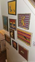 Nine framed needlepoint artworks of various animals and scenes hanging on a wall.